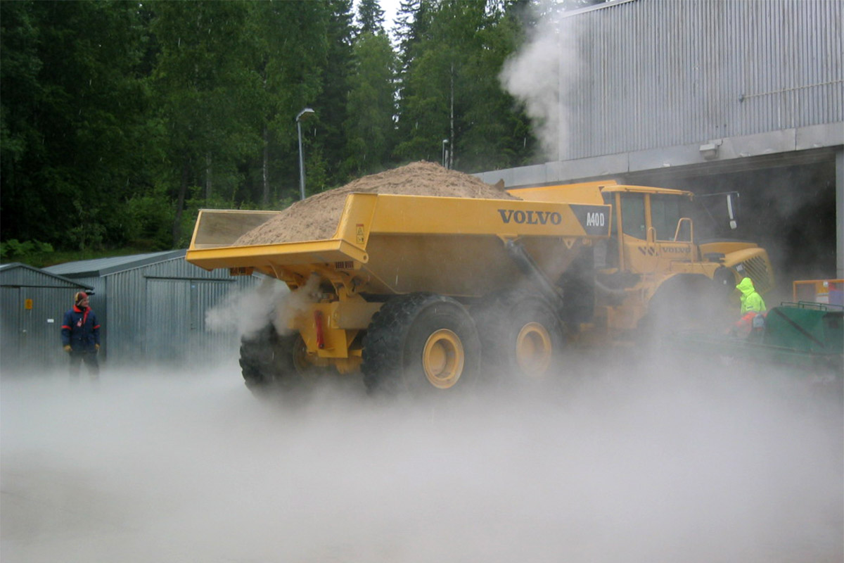 A yellow Volvo dumper with mist around it, in front of a building 